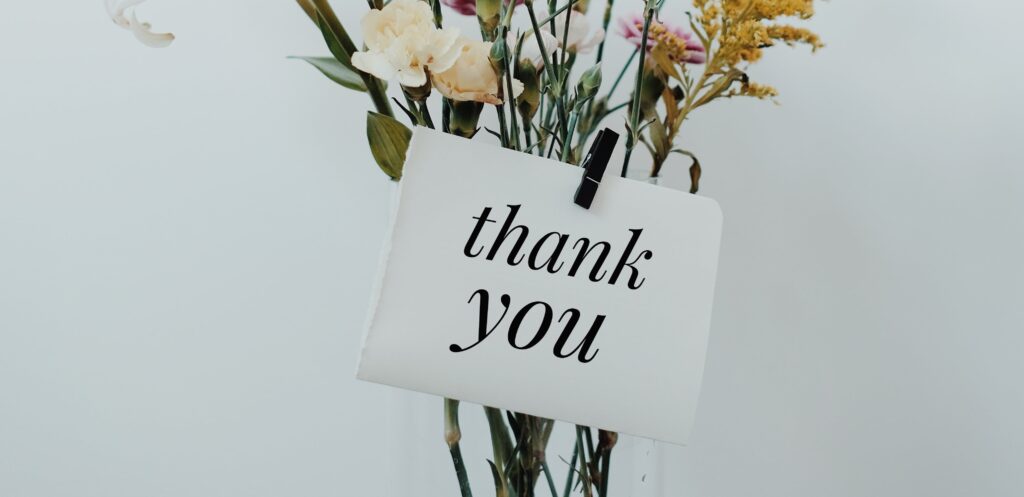 [Image description: a card with 'thank you' script, attached to a vase of flowers]